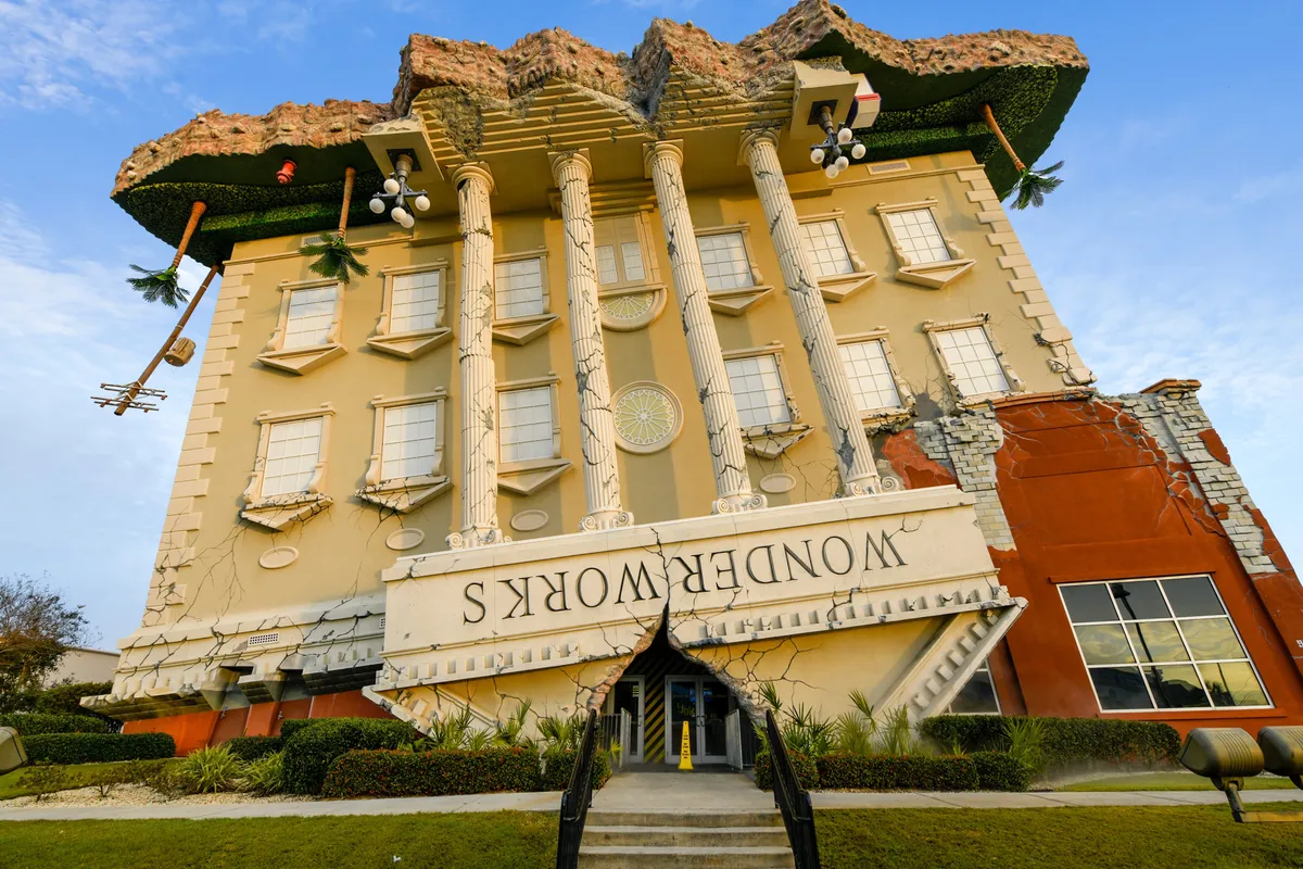 The striking upside-down WonderWorks building, with classical columns and a whimsical design, stands out with its tilted windows, palm trees, and bold signage. The playful exterior invites curiosity and promises unique, interactive experiences inside.