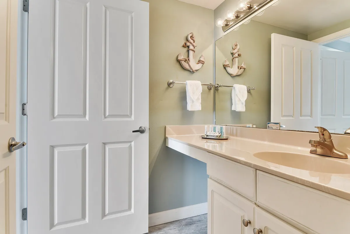A serene bathroom with a well-lit vanity, a modern sink, a large mirror, and decorative anchors on the wall. The pale tones and inviting setup evoke a spa-like environment that encourages relaxation and self-care.