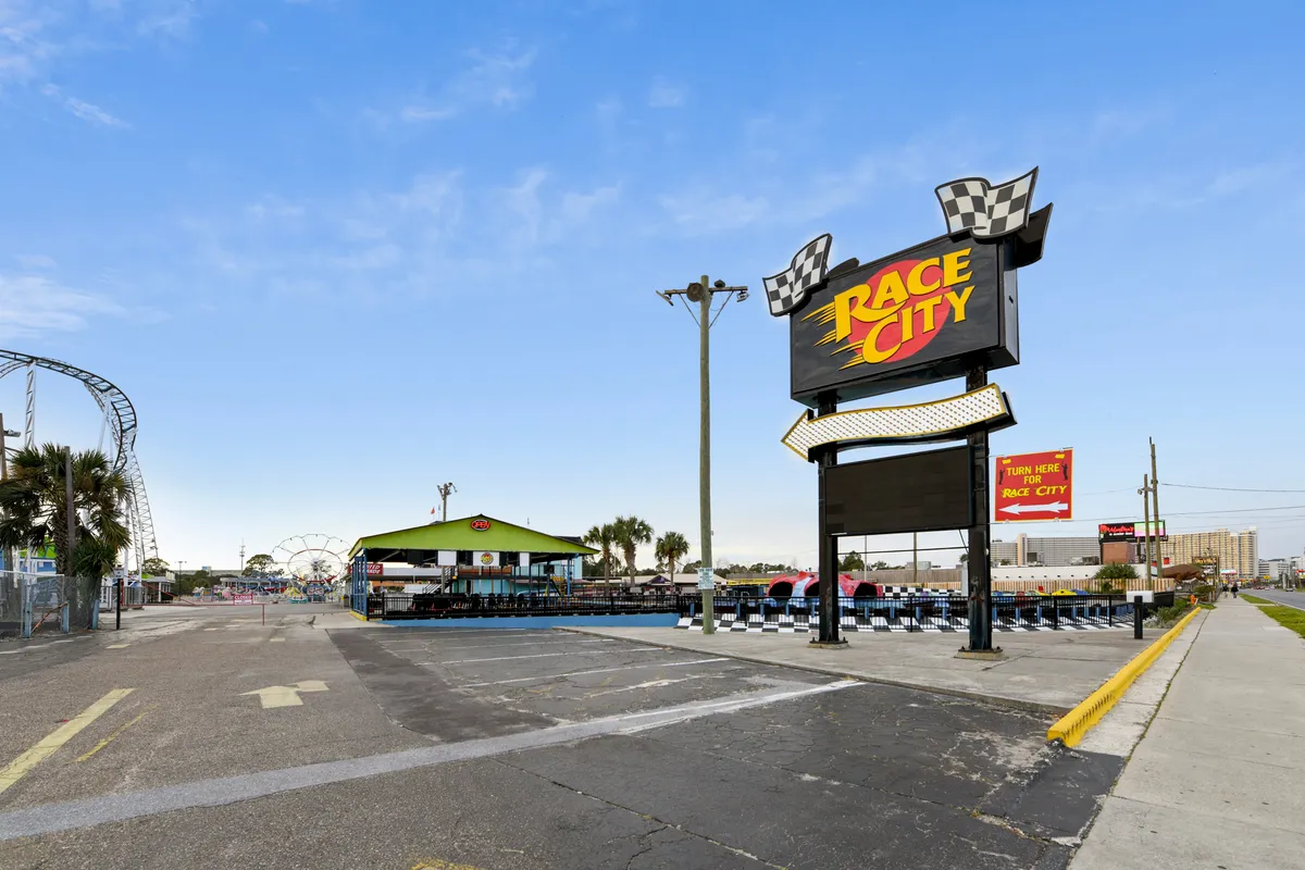This dynamic exterior shot showcases the vibrant Race City attraction, with its bright sign, go-kart track, Ferris wheel, and a lively seating area bustling with excitement.