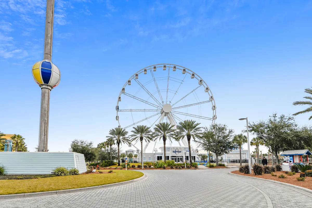 This image features the iconic Ferris wheel at Pier Park, with palm trees and the entrance building in the foreground. The atmosphere is lively and inviting, capturing a classic Panama City Beach experience.